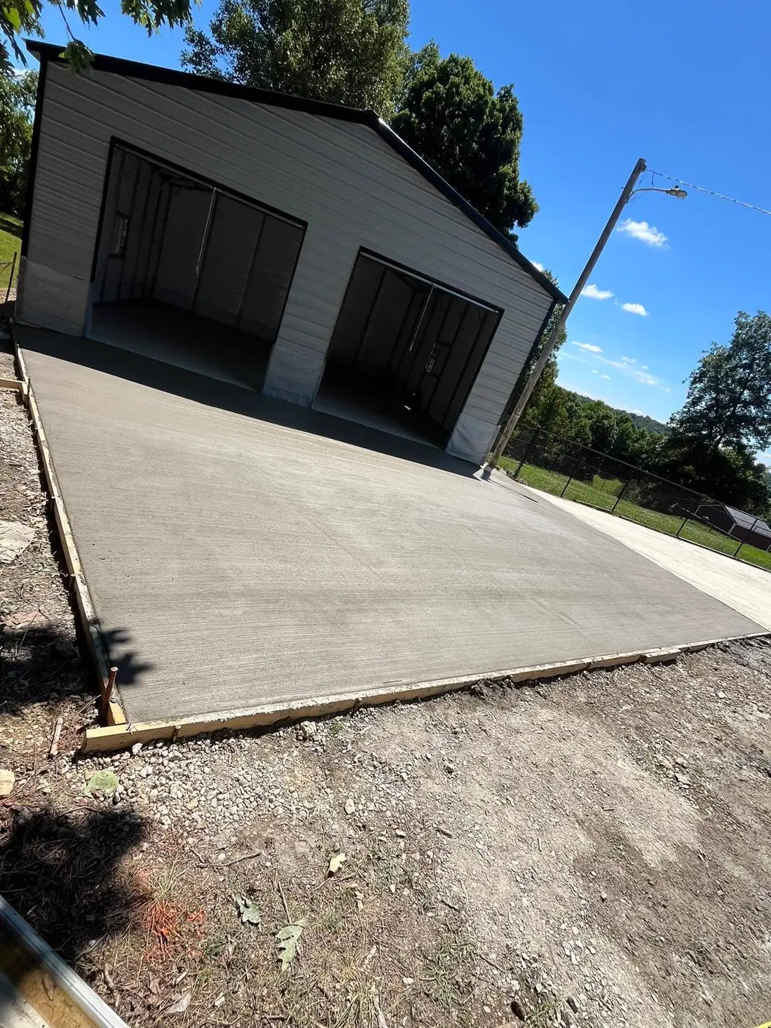 Concrete driveway and garage pad poured beside a black garage